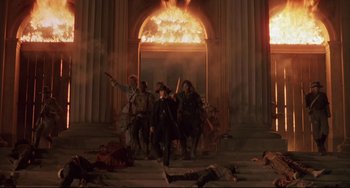 Movie still from “Walker” (1987), directed by Alex Cox – A group of people standing in front of a fire; Wide shot, Low angle