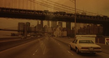Movie still from “Wall Street” (1987), directed by Oliver Stone – A car driving on a highway with a bridge in the background; Extreme Wide shot, High angle