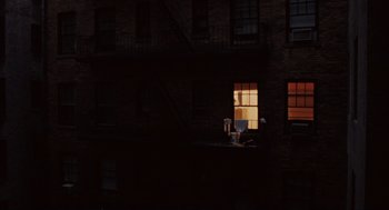 Movie still from “Wall Street” (1987), directed by Oliver Stone – A person sitting on a window sill in a dark room; Extreme Wide shot, High angle