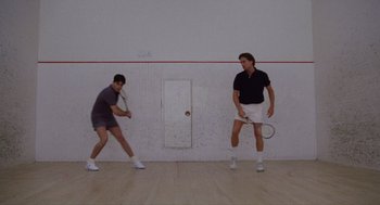 Movie still from “Wall Street” (1987), directed by Oliver Stone – Two men are playing a game of squash on the court; Wide shot, Low angle