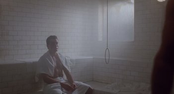 Movie still from “Wall Street” (1987), directed by Oliver Stone – A man sitting on a bench in a room with white tile walls; Medium shot, Low angle