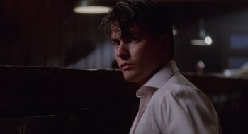 Movie still from “Wall Street” (1987), directed by Oliver Stone – A man in a white dress shirt is standing in a dark room; Close Up shot, Low angle