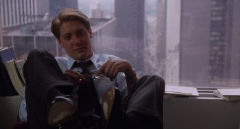 Movie still from “Wall Street” (1987), directed by Oliver Stone – A man sitting in front of a window with a tie; Medium shot, High angle