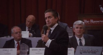 Movie still from “Wall Street” (1987), directed by Oliver Stone – A man in a suit and tie holding a microphone; Medium shot, Over the shoulder angle