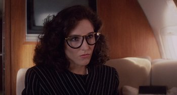 Movie still from “Wall Street” (1987), directed by Oliver Stone – A woman wearing glasses sitting on top of a couch; Close Up shot, Over the shoulder angle