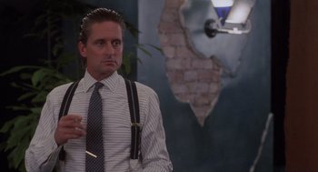 Movie still from “Wall Street” (1987), directed by Oliver Stone – A man smoking a cigarette in a room; Medium shot, Over the shoulder angle