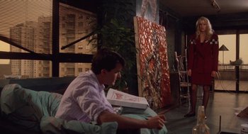 Movie still from “Wall Street” (1987), directed by Oliver Stone – A man sitting in a chair holding a pizza box; Wide shot, Over the shoulder angle