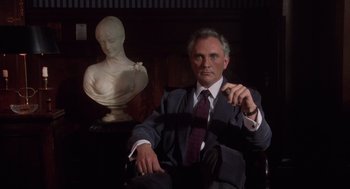 Movie still from “Wall Street” (1987), directed by Oliver Stone – A man sitting in a chair in front of a bust; Medium shot, Low angle