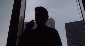 Movie still from “Wall Street” (1987), directed by Oliver Stone – A man smoking a cigarette in front of a window; Medium shot, Low angle