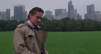 Movie still from “Wall Street” (1987), directed by Oliver Stone – A man in a trench coat and tie standing in a field; Medium shot, Over the shoulder angle