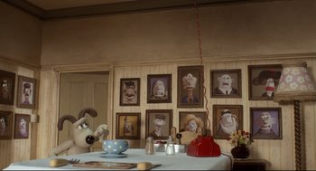 Movie still from “Wallace & Gromit: The Curse of the Were-Rabbit” (2005), directed by Nick Park – A table in front of a bunch of pictures of wallace and gromit; Wide shot, High angle
