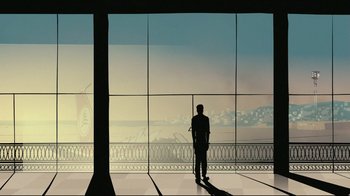 Movie still from “Waltz with Bashir” (2008), directed by Ari Folman – A man standing in front of a large window looking out at a city skyline; Wide shot, Low angle