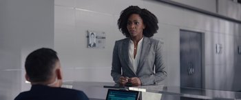 Movie still from “WandaVision” (2021), directed by Matt Shakman – A woman in a gray suit is standing in front of a laptop; Medium shot, Over the shoulder angle