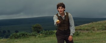 Movie still from “War Horse” (2011), directed by Steven Spielberg – A man holding an apple while standing in a field; Medium shot, Low angle