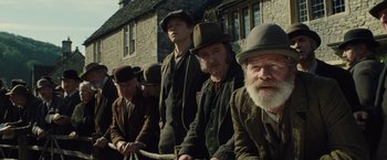 Movie still from “War Horse” (2011), directed by Steven Spielberg – A group of men in hats and coats sitting in front of a building; Medium shot, Low angle