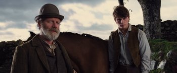 Movie still from “War Horse” (2011), directed by Steven Spielberg – A man standing next to a horse and another man standing next to a horse; Medium shot, Low angle