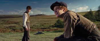 Movie still from “War Horse” (2011), directed by Steven Spielberg – A man with a hat is sitting in the grass; Medium shot, Low angle