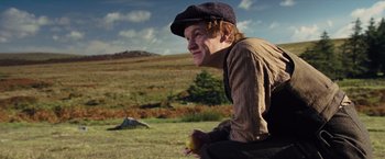 Movie still from “War Horse” (2011), directed by Steven Spielberg – A young man holding an apple while sitting in a field; Medium shot, Low angle