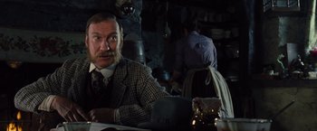 Movie still from “War Horse” (2011), directed by Steven Spielberg – A man sitting at a table in front of other people; Medium shot, Low angle