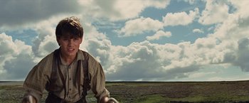 Movie still from “War Horse” (2011), directed by Steven Spielberg – A man in a plaid shirt and a hat standing in front of a field; Medium shot, Low angle