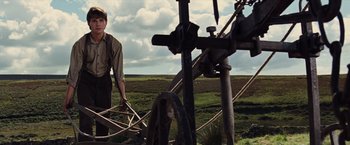 Movie still from “War Horse” (2011), directed by Steven Spielberg – A man standing in a field holding a large metal object; Medium shot, Low angle