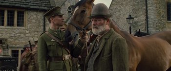 Movie still from “War Horse” (2011), directed by Steven Spielberg – A man in a suit and hat standing next to a horse; Medium shot, Low angle