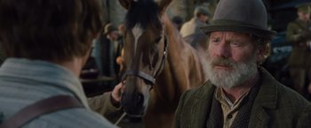 Movie still from “War Horse” (2011), directed by Steven Spielberg – A man with a beard and a hat standing next to a brown horse; Close Up shot, Over the shoulder angle