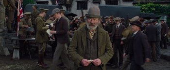 Movie still from “War Horse” (2011), directed by Steven Spielberg – An old man in a hat and a suit is standing in front of a group of people; Medium shot, Low angle