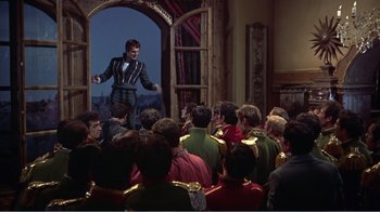 Movie still from “War and Peace” (1956), directed by King Vidor – A group of people sitting in front of a man in a suit; Wide shot, Over the shoulder angle