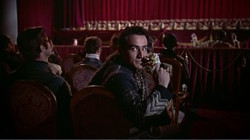 Movie still from “War and Peace” (1956), directed by King Vidor – A man sitting in front of a curtain holding a cell phone; Medium shot, Over the shoulder angle