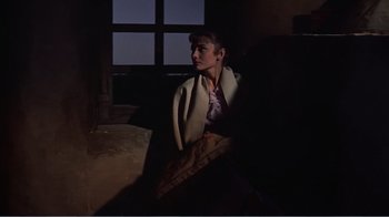 Movie still from “War and Peace” (1956), directed by King Vidor – A woman wrapped in a blanket sitting on a couch; Medium shot, Over the shoulder angle