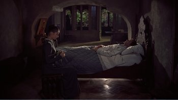 Movie still from “War and Peace” (1956), directed by King Vidor – A woman sitting on a chair next to a man in a bed; Wide shot, High angle