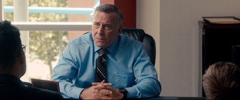 Movie still from “War on Everyone” (2016), directed by John Michael McDonagh – A man sitting at a desk wearing a blue dress shirt and tie; Close Up shot, Over the shoulder angle