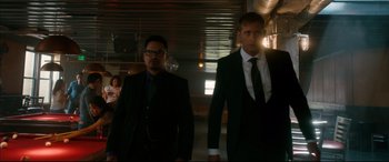 Movie still from “War on Everyone” (2016), directed by John Michael McDonagh – A man in a suit and tie standing next to another man in a suit and tie; Medium shot, Low angle