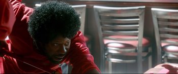 Movie still from “War on Everyone” (2016), directed by John Michael McDonagh – A man with a red shirt and a black afro; Close Up shot, Over the shoulder angle