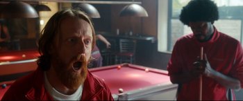 Movie still from “War on Everyone” (2016), directed by John Michael McDonagh – A man with red hair and a beard is playing a game of billiards; Close Up shot, Over the shoulder angle