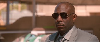 Movie still from “War on Everyone” (2016), directed by John Michael McDonagh – A person wearing a suit and sunglasses; Close Up shot, Low angle