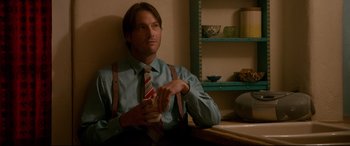 Movie still from “War on Everyone” (2016), directed by John Michael McDonagh – A man sitting at a table with a drink in his hand; Medium shot, Over the shoulder angle