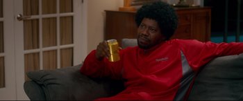 Movie still from “War on Everyone” (2016), directed by John Michael McDonagh – A man sitting on a couch holding a can of beer; Medium shot, Over the shoulder angle