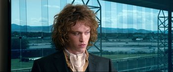 Movie still from “War on Everyone” (2016), directed by John Michael McDonagh – A man with long curly hair wearing a suit and tie; Close Up shot, Over the shoulder angle