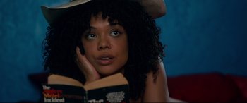 Movie still from “War on Everyone” (2016), directed by John Michael McDonagh – A beautiful young lady reading a book while laying down with her head resting on her hand; Close Up shot, Over the shoulder angle