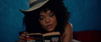 Movie still from “War on Everyone” (2016), directed by John Michael McDonagh – A woman in a white hat is reading a book; Close Up shot, High angle