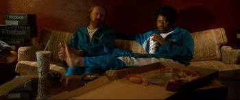 Movie still from “War on Everyone” (2016), directed by John Michael McDonagh – Two men sitting on a couch with pizza on the table; Medium shot, High angle
