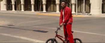 Movie still from “War on Everyone” (2016), directed by John Michael McDonagh – A man in a bright red outfit stands next to a bicycle; Medium shot, Over the shoulder angle