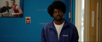 Movie still from “War on Everyone” (2016), directed by John Michael McDonagh – A man in a blue jacket with a black afro; Close Up shot, Over the shoulder angle