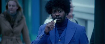 Movie still from “War on Everyone” (2016), directed by John Michael McDonagh – A man in a blue suit eating a piece of food; Medium shot, Low angle