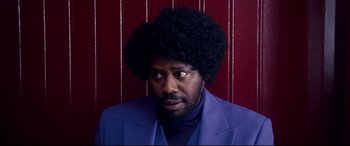 Movie still from “War on Everyone” (2016), directed by John Michael McDonagh – A man in a purple suit with a black afro; Close Up shot, Low angle
