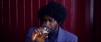 Movie still from “War on Everyone” (2016), directed by John Michael McDonagh – A man in a purple suit drinking from a glass; Close Up shot, Low angle