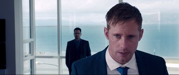 Movie still from “War on Everyone” (2016), directed by John Michael McDonagh – A man in a suit standing next to another man in a suit; Close Up shot, Over the shoulder angle