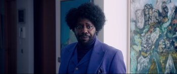 Movie still from “War on Everyone” (2016), directed by John Michael McDonagh – A man in a blue suit and a black afro; Medium shot, Over the shoulder angle
